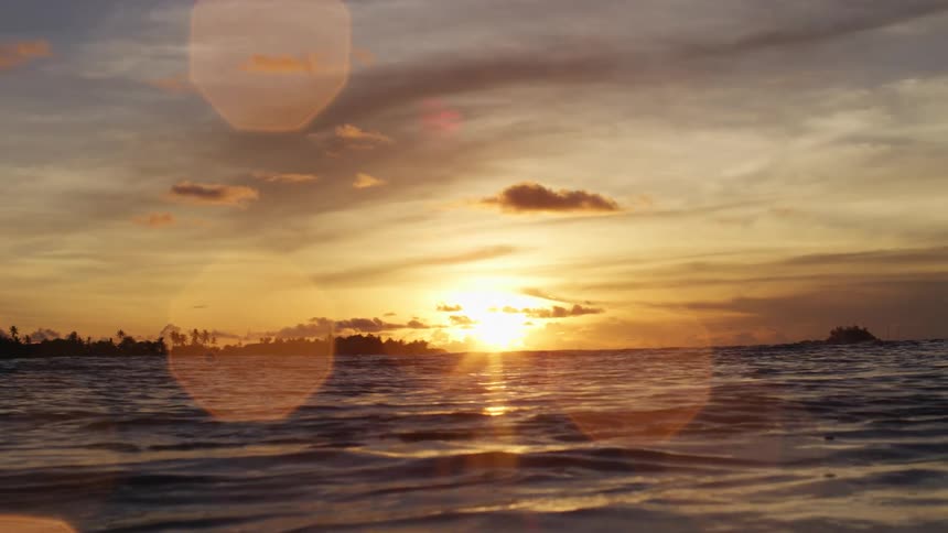 A body of water with waves with the sunset the sky and clouds in the background