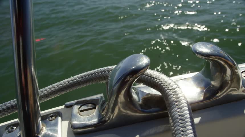 Rope is fastened to boat and as boat cuts through water reflecting sunlight