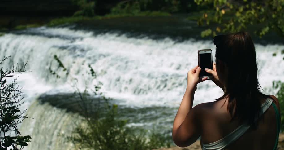 A woman uses her smartphone to record video of a waterfall