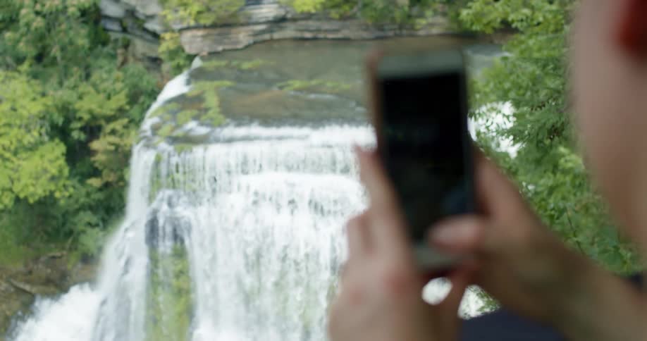 A woman films a large waterfall with her phone