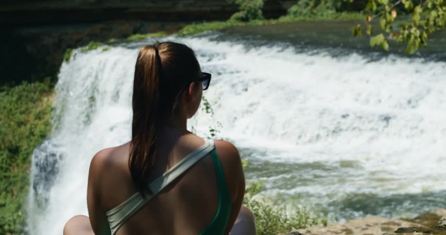 A teenage girl sits and watches a waterfall