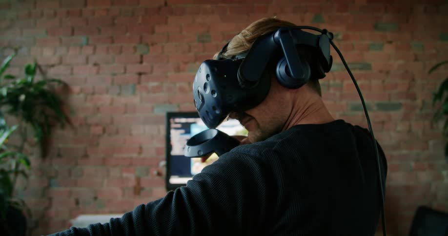 A man wearing a virtual reality headset stands and aims his attack within the video game