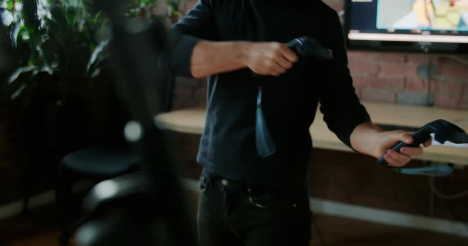 A man with a vr headset standing in a room with a monitor and a wall in the background