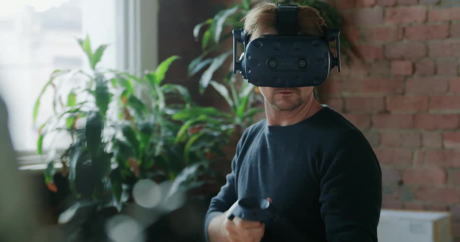 Man wearing vr goggles walks back and forth next to brick wall and wall mounted television