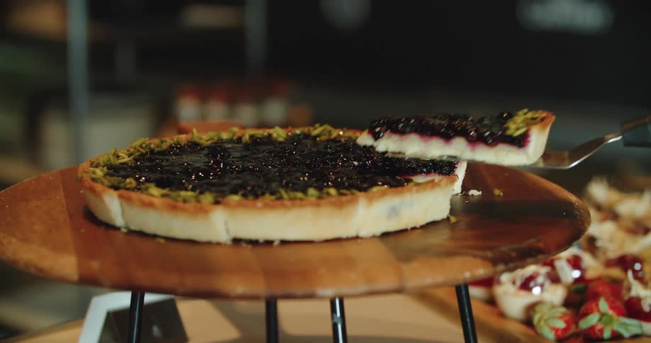 A bakery employee removes a slice of blueberry tart from a display