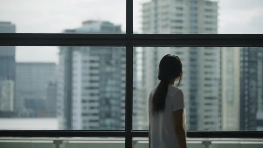 A woman looks out the window at the office buildings across the street