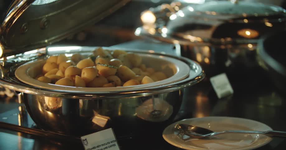 A person opening up a pot of potatoes on a table with a spoon and plate