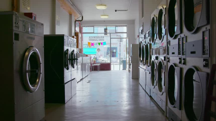 An aisle lined with washing machines and dryers but devoid of people in a laundromat during the day