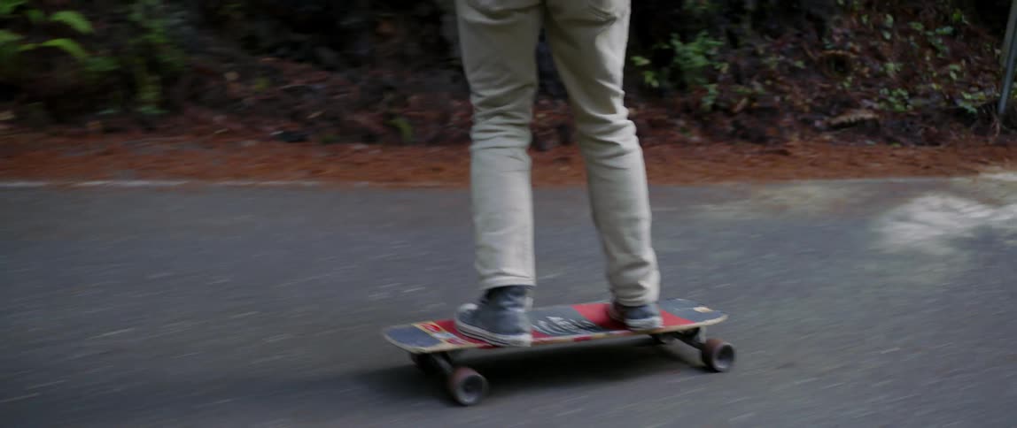 A man in a blue plaid shirt rides a skateboard down a hill