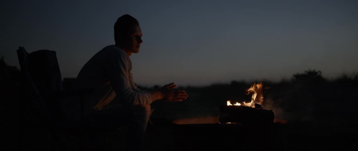 Man sitting and warming his hands by a campfire