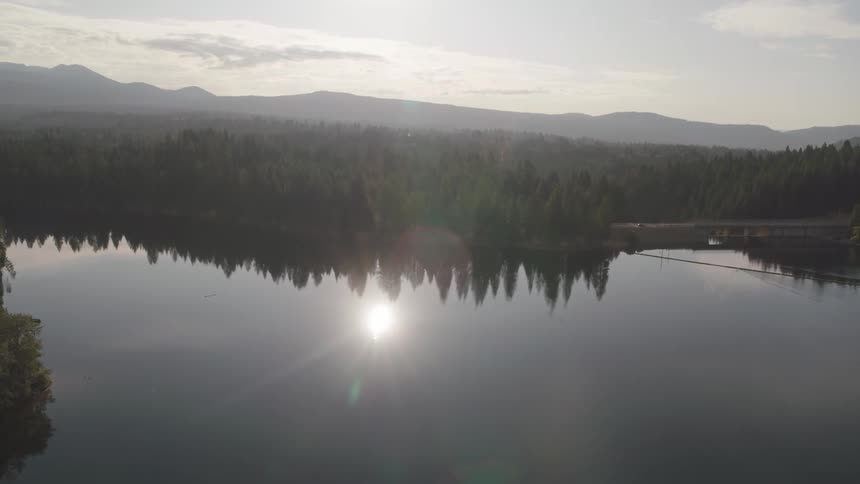 A calm lake surrounded by forest reflects the clear morning sky