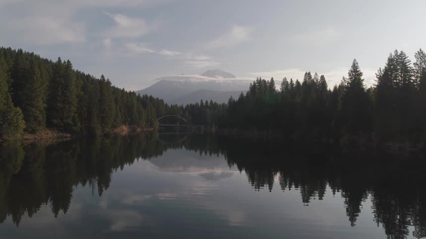 An aerial view of a lake with trees on both sides and a mountain in the background