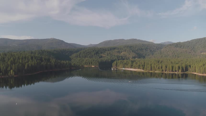 Aerial view of a tranquil lake with mountain forests on a sunny day