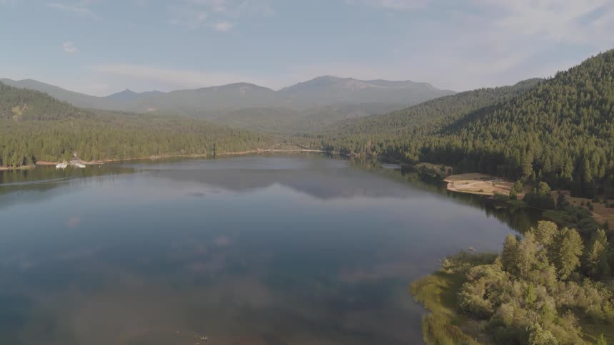 A lake surrounded by trees with a mountain range the sky and clouds in the background