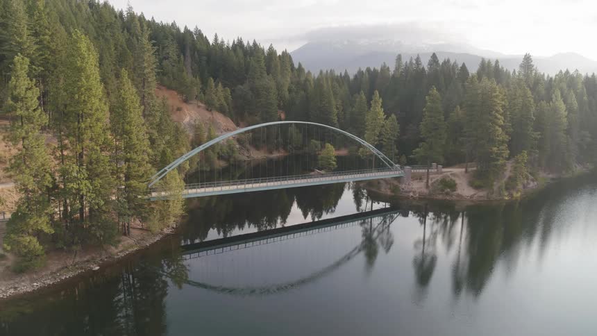 An aerial view of a bridge crossing a lake into a forest