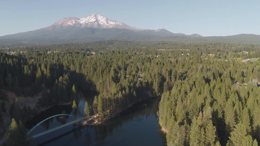 An aerial view of a forest lake with a snowy mountain in the distance