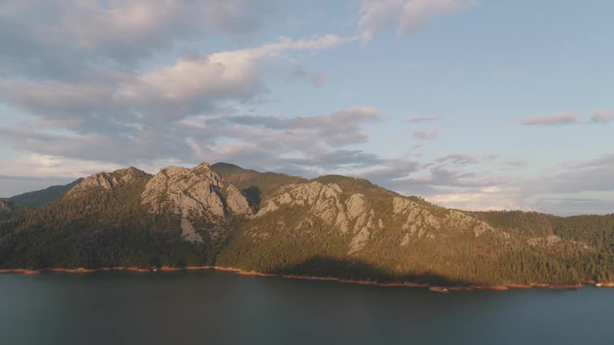 Aerial view of a tranquil lake with mountain forests against the blue sky