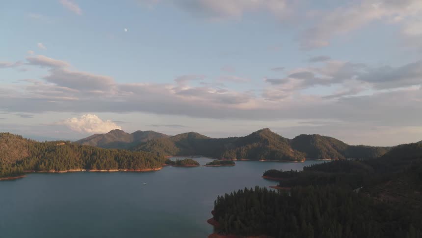 A boat moves across a large lake near mountain ranges