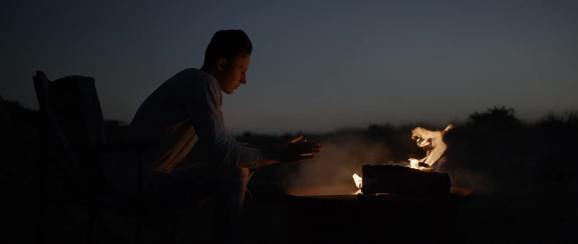 A man warms his hands on a fire at night