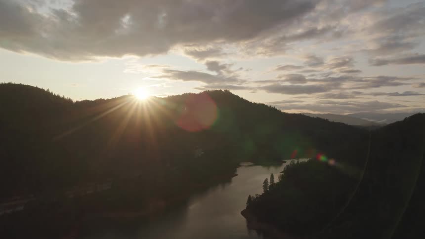 A river surrounded by trees with a mountain range a sunset the sky and clouds in the background