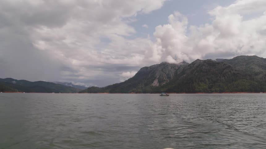 Small boat on large lake in front of mountains
