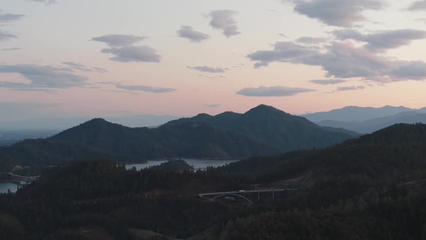 A bridge with vehicles with a lake a mountain range and the sky in the background