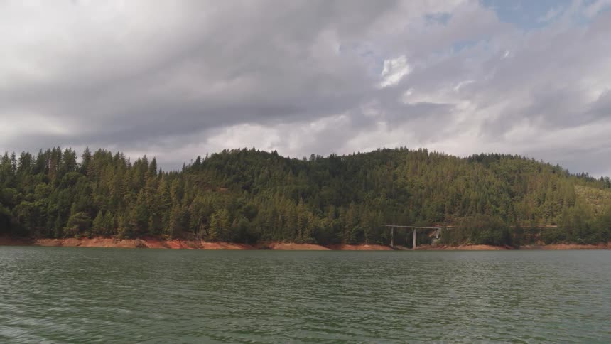 View of a tranquil lake with a mountain forest on a cloudy day