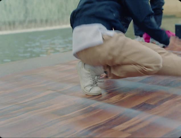 A young asian woman break dances on a dance mat in front of a fountain in a public park as spectators watch