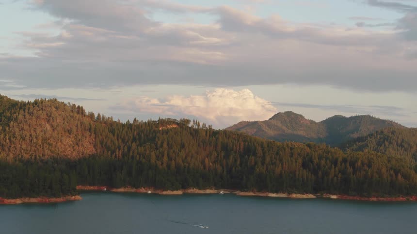 A lake surrounded by mountain and forest under a cloudy daytime sky