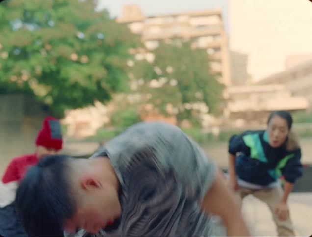 A male dancer is break dancing in a park on a mat while a man and woman are watching on the sides
