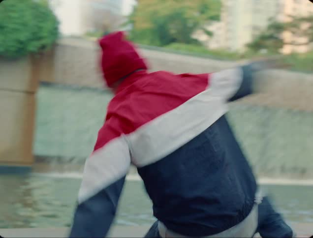 A teenage boy breakdances in front of a fountain in a public park as others watch