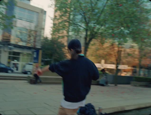 A female dancer switches places with a male dancer and dances in front of a fountain in a park