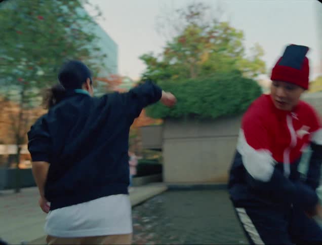 Two men and a woman dancing next to a fountain with buildings and the sky in the background