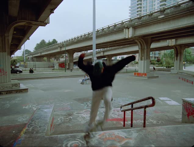 A skateboarder attempts to flip his skateboard while jumping down a staircase but fails and stumbles