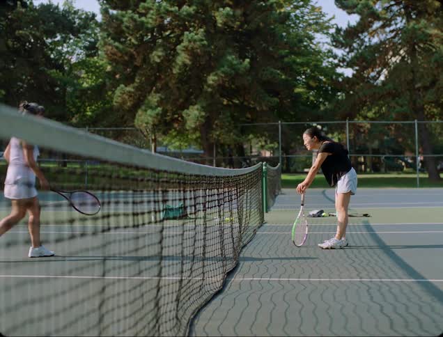 Two women come to the center net of a tennis court and look tired