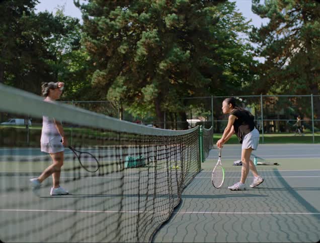 Two women walk to the tennis court net and then turn and walk off of the court