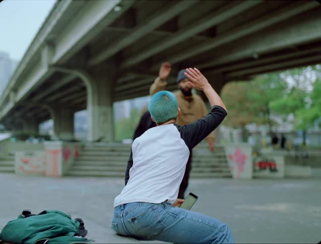 A person sits on a ledge and high fives fellow skateboarders passing by