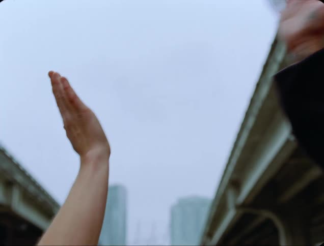 A man with a hat passing by and giving a fake high five to another person with buildings the sky and clouds in the background