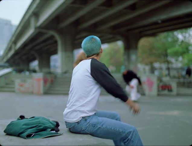 A person sitting in a skate park with buildings trees and an overpass in the background