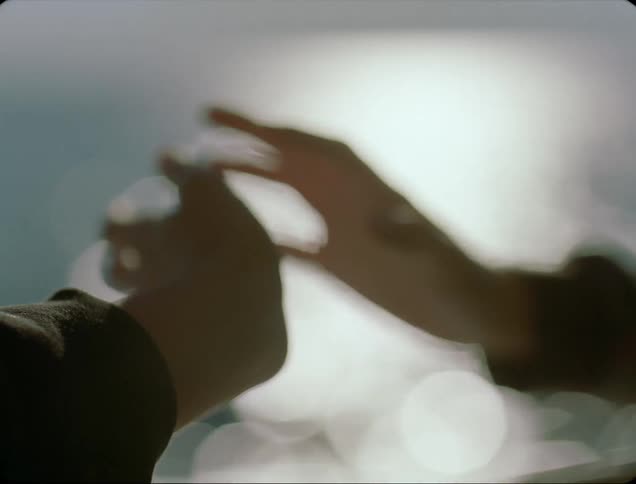 Two people moving their hands with the ocean and sunlight reflecting off the water in the background