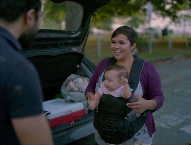 A man walks across a parking lot to greet a woman and her baby