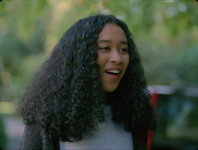 Black girl with curly hair smiles brightly and talks to person