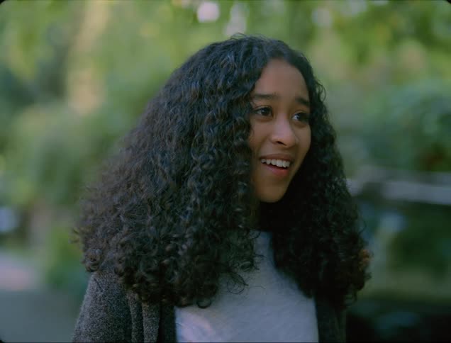 Black girl with curly hair laughs and talks to person