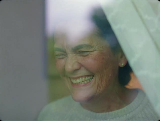A woman smiles then waves and blows kisses while facing a window
