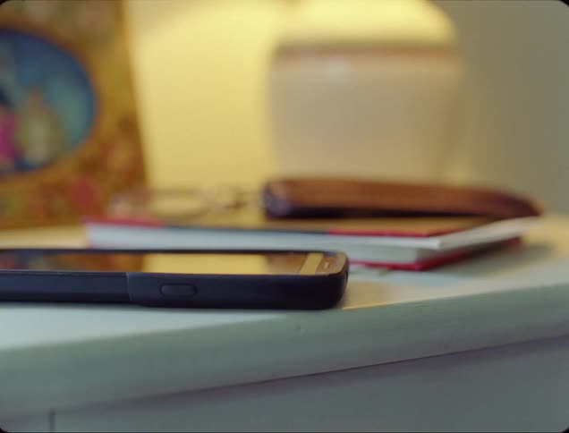 A nightstand with a smart phone a book a picture frame and a lamp
