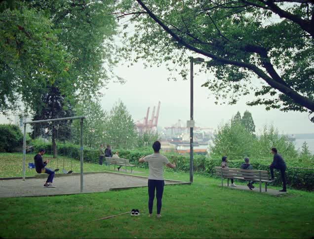 People stand and sit frozen at a playground and park near a shipyard by the sea