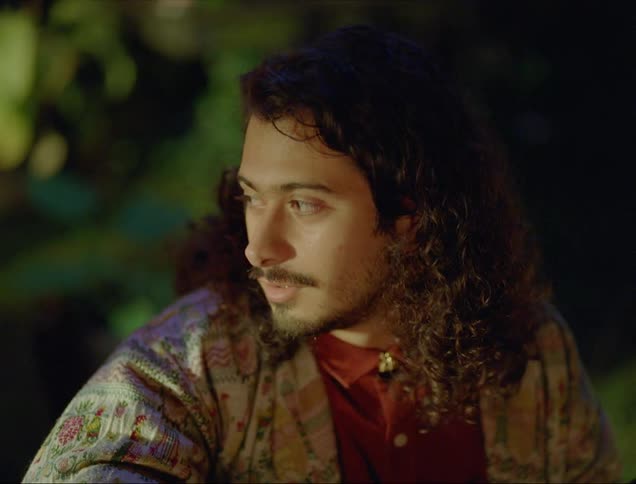 A man sits at a table lost in thought before gesturing and nodding at someone out of frame