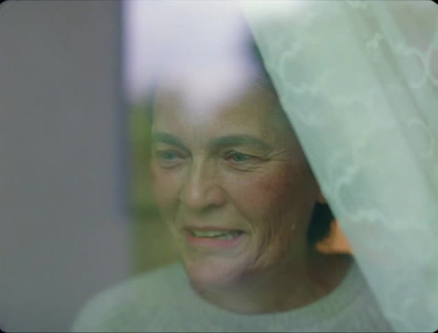 An elderly woman looks shocked when she looks out her window and then she smiles and laughs and blows kisses