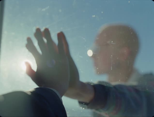 A man has his hand resting on a window and a woman on the other side puts her hand against his