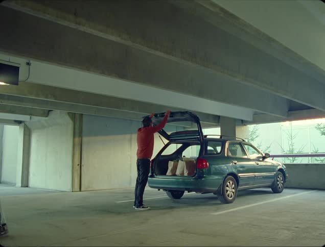 A store employee helps a man load shopping bags into the trunk of his vehicle in a parking garage